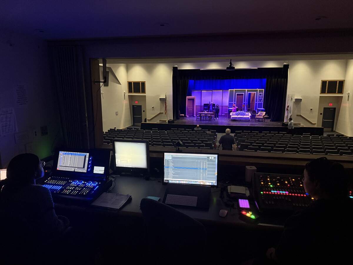 Inside the dark tech booth, the crew readies for rehearsals as the actors prepare on stage below.
